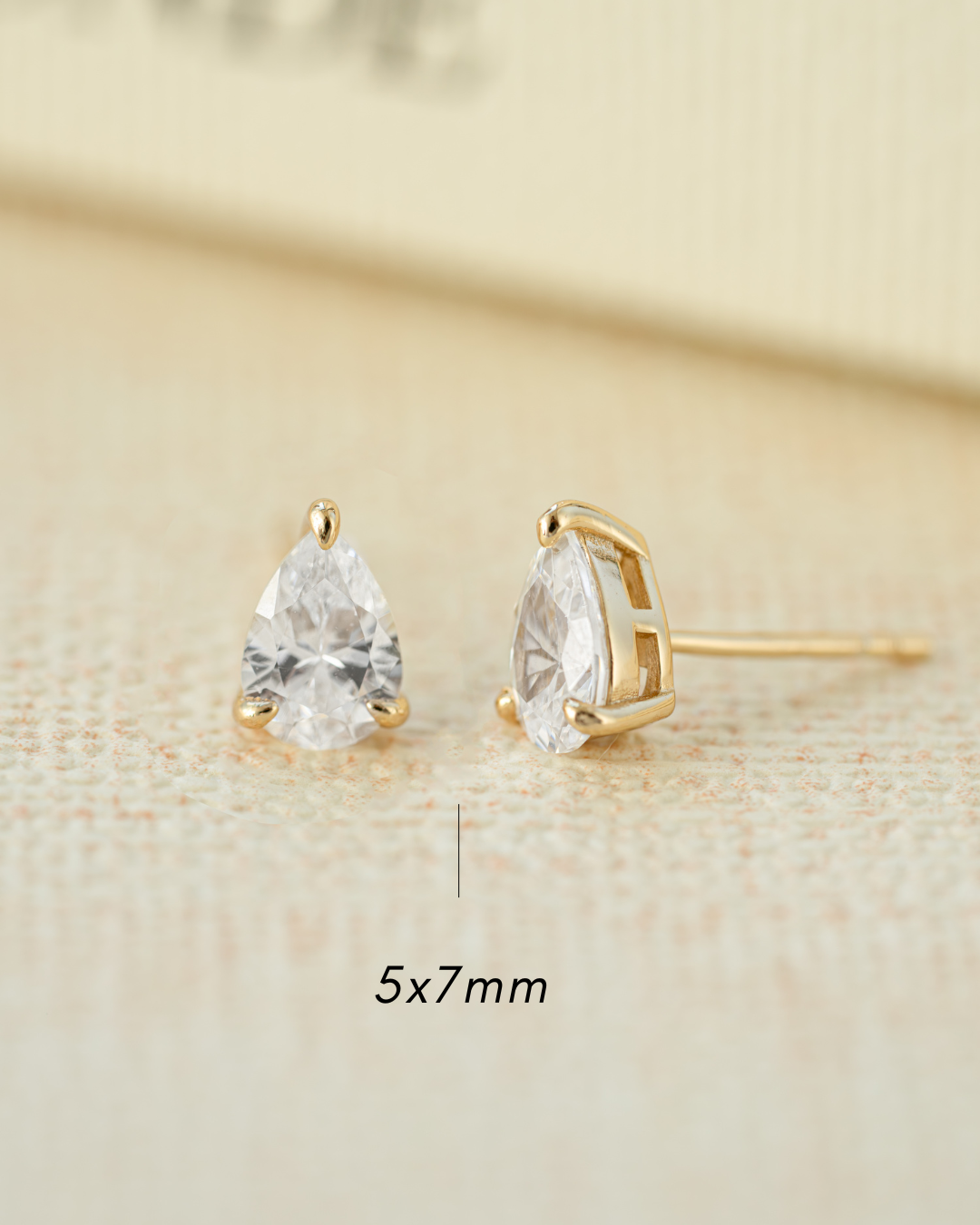 Gold cubic zirconia earrings on a beige background with a 5x7mm measurement 