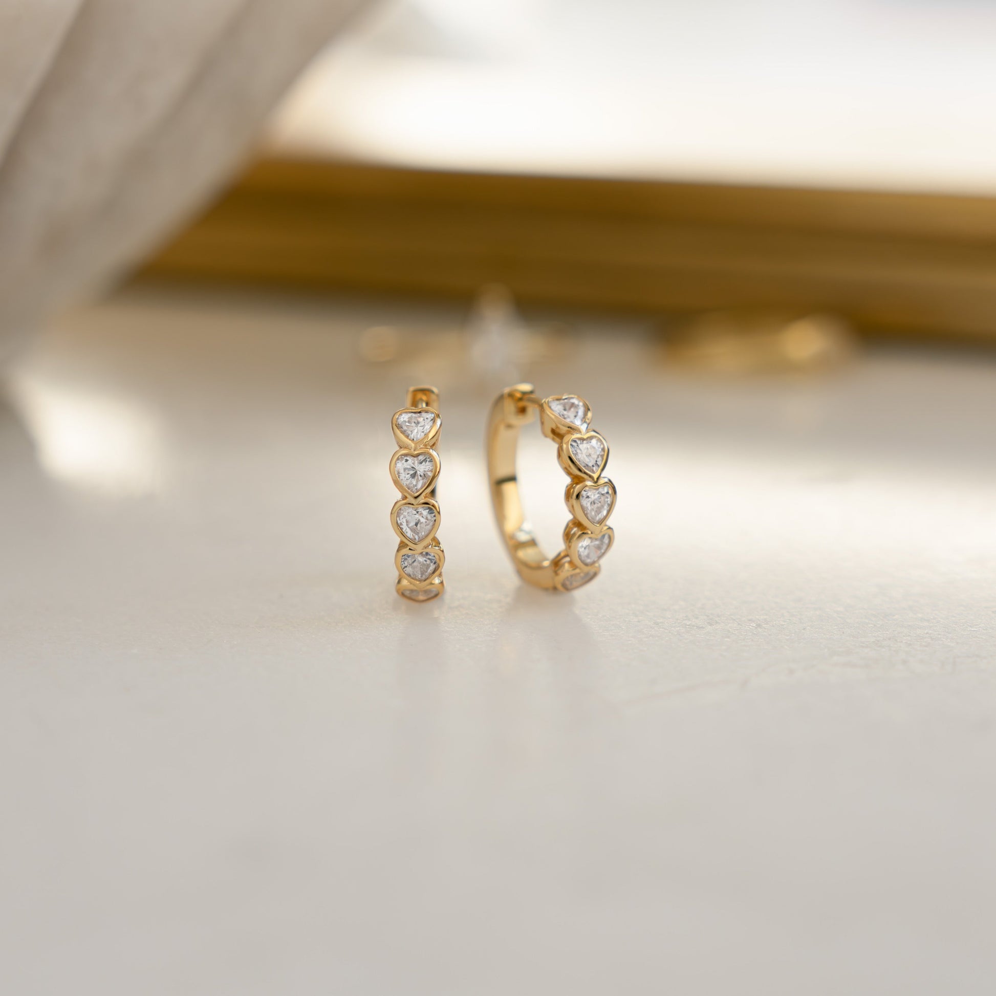 close up of small gold hoop earrings with delicate heart accents.