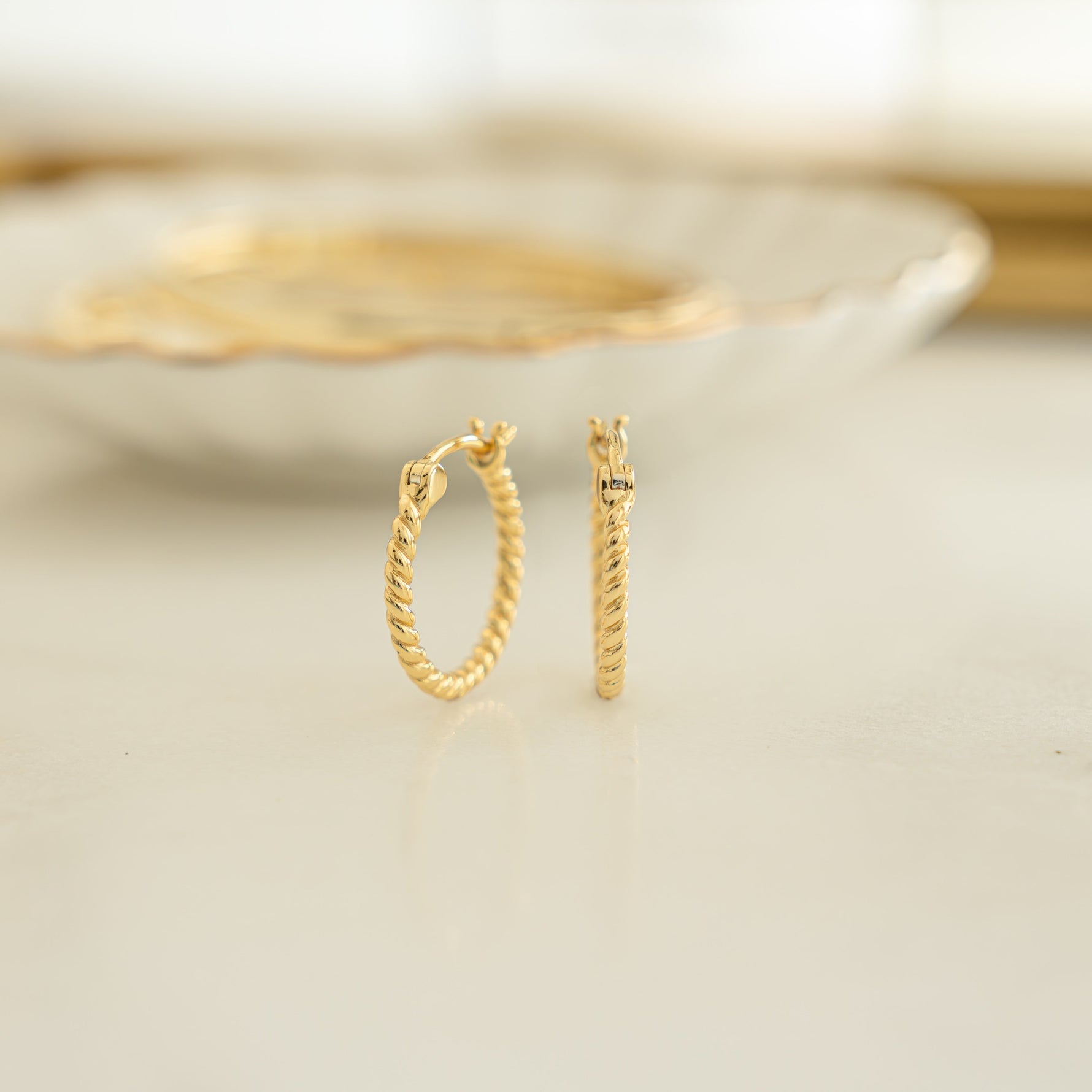 Closeup image of dainty gold hoop earrings with spiral design