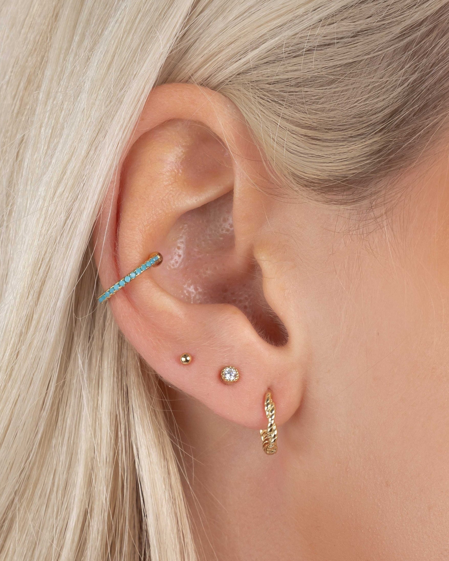Mini gold hoop earrings, with a twisted hoop earring design, diamond stud earring, a gold ball stud earring, and a turquoise ear cuff