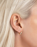 Close-up of a person wearing gold hoop earrings, gold bezel set diamond stud earrings and a ball stud 