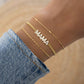 Model showcasing gold jewelry featuring charm bracelet with MAMA charm and gold chain 