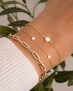 dainty gold bracelets on model featuring a dainty opal chain bracelet, a opal beaded bracelet, and a pave paperclip bracelet all in gold