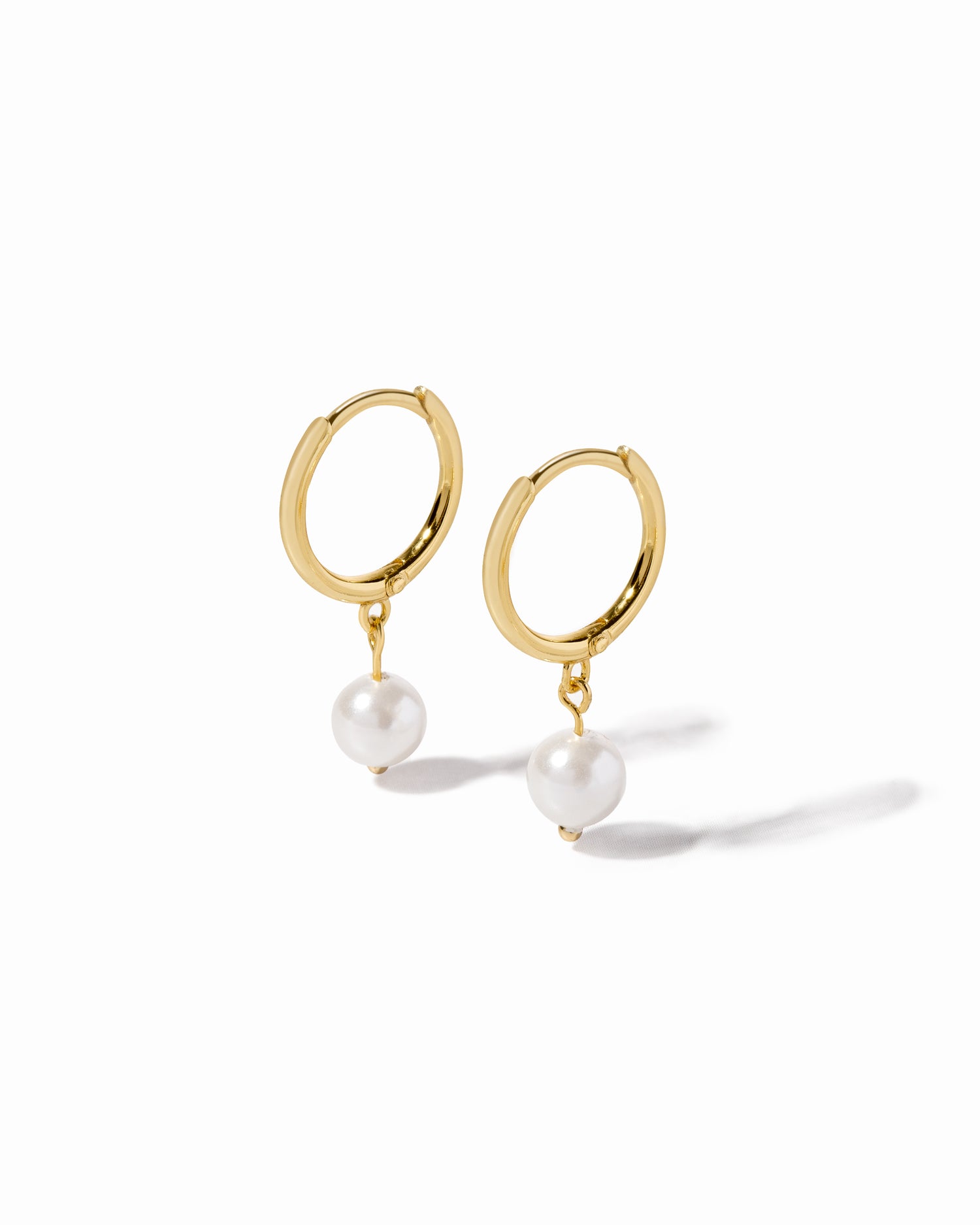 Gold hoop earrings with pearl drops on a white background