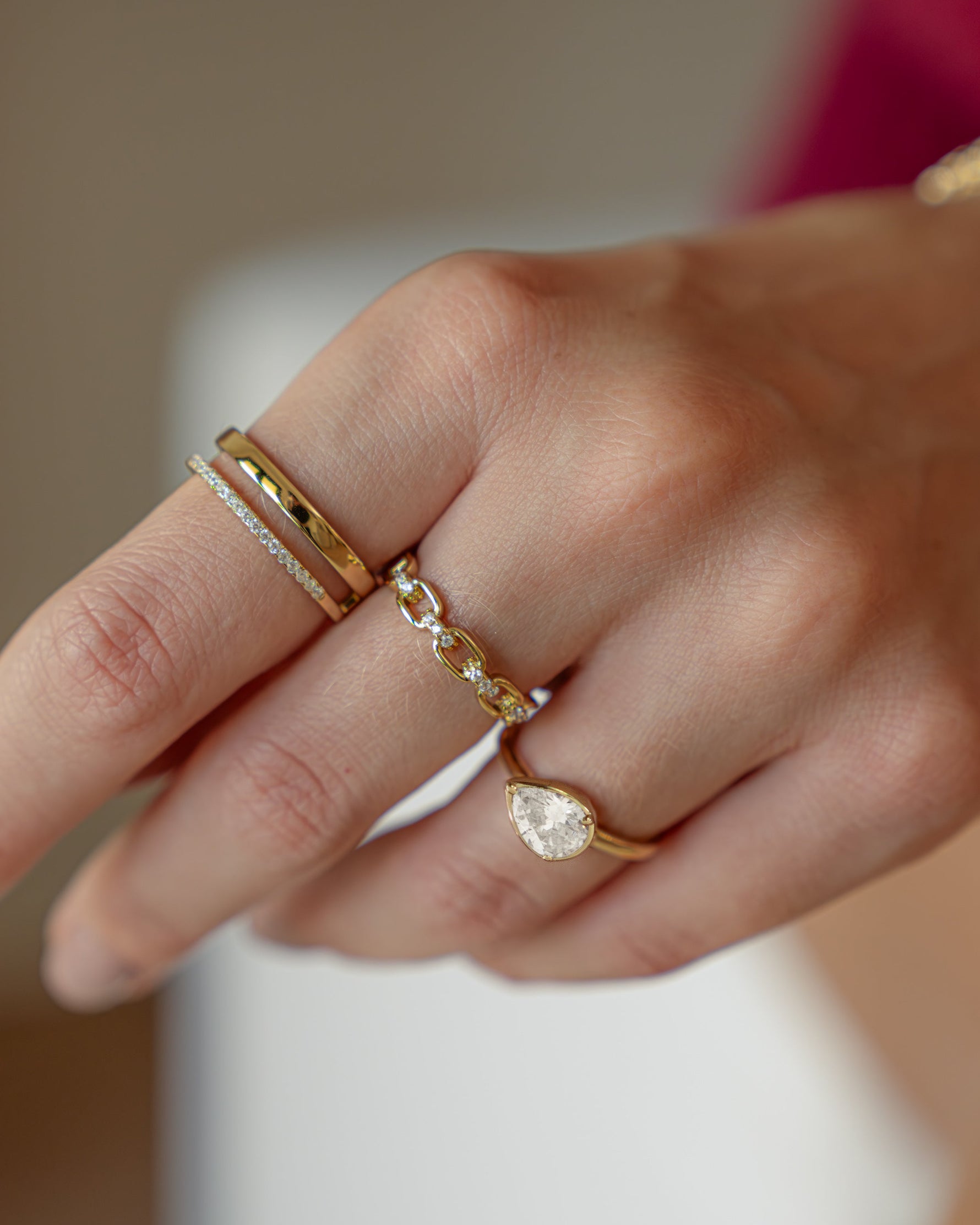 Model wearing dainty gold stackable rings featuring a pear ring, a chain ling ring, and a gold double band statement ring