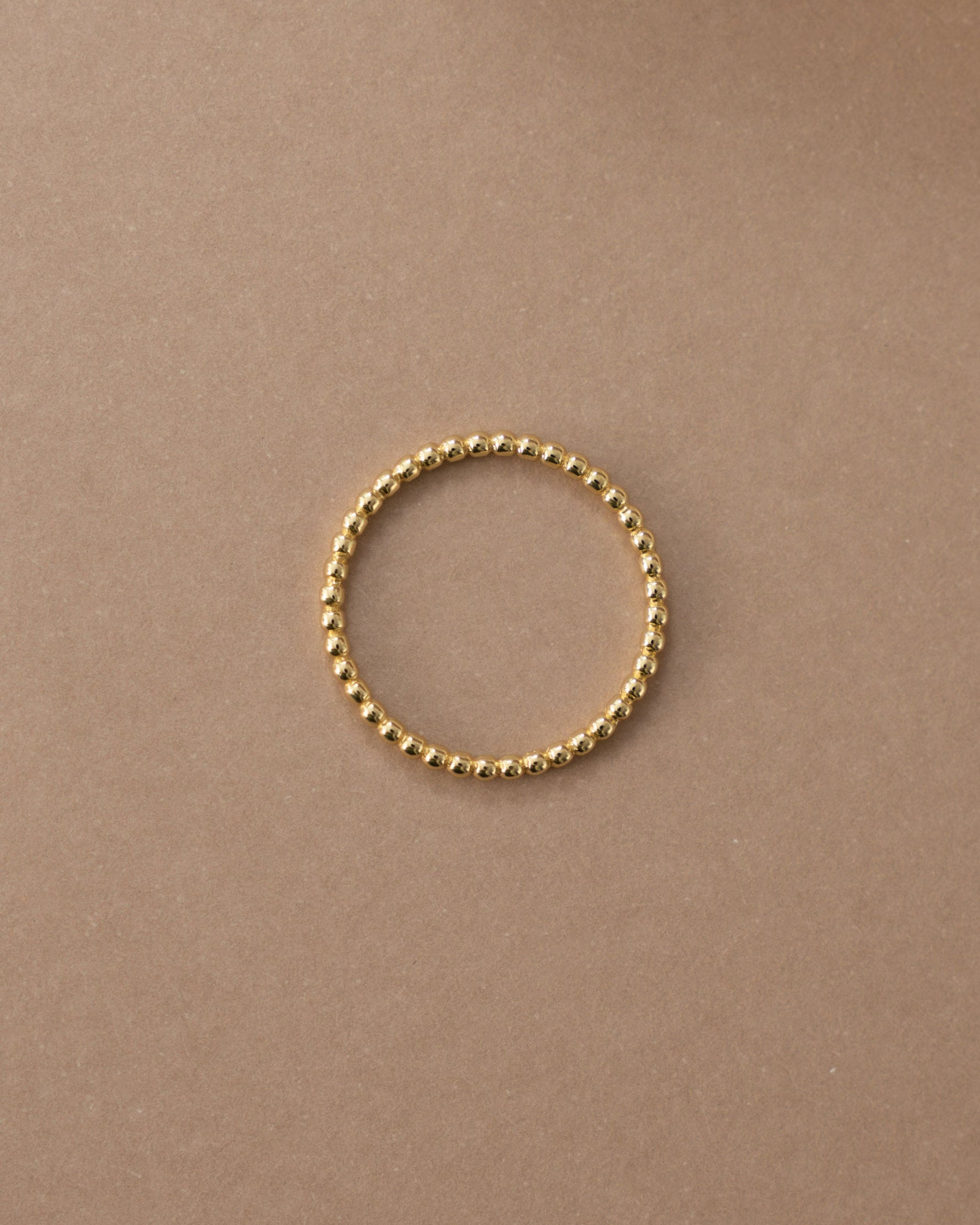 Gold plain beaded ring on a beige surface 