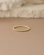 Gold plain beaded ring on a beige surface
