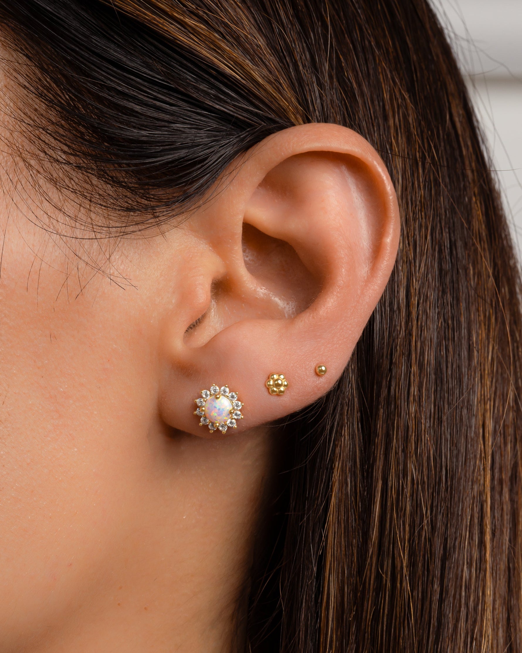 A model's ear with opal and gold flower stud earrings.