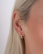 Close-up of a model wearing three gold earrings including a pair of dainty huggie hoops, minimalist stud earrings, and small ball studs