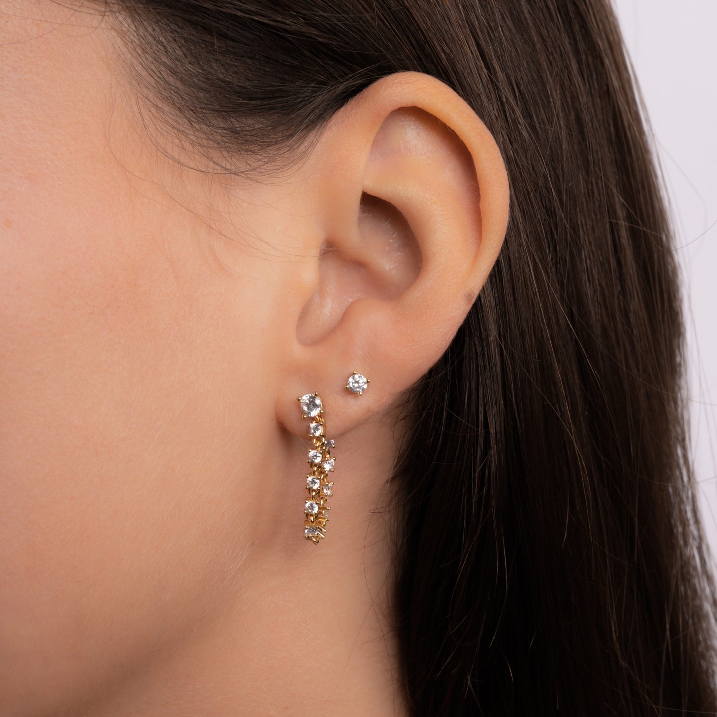 Close-up of gold chain drop earrings and diamond stud earrings worn by the model.