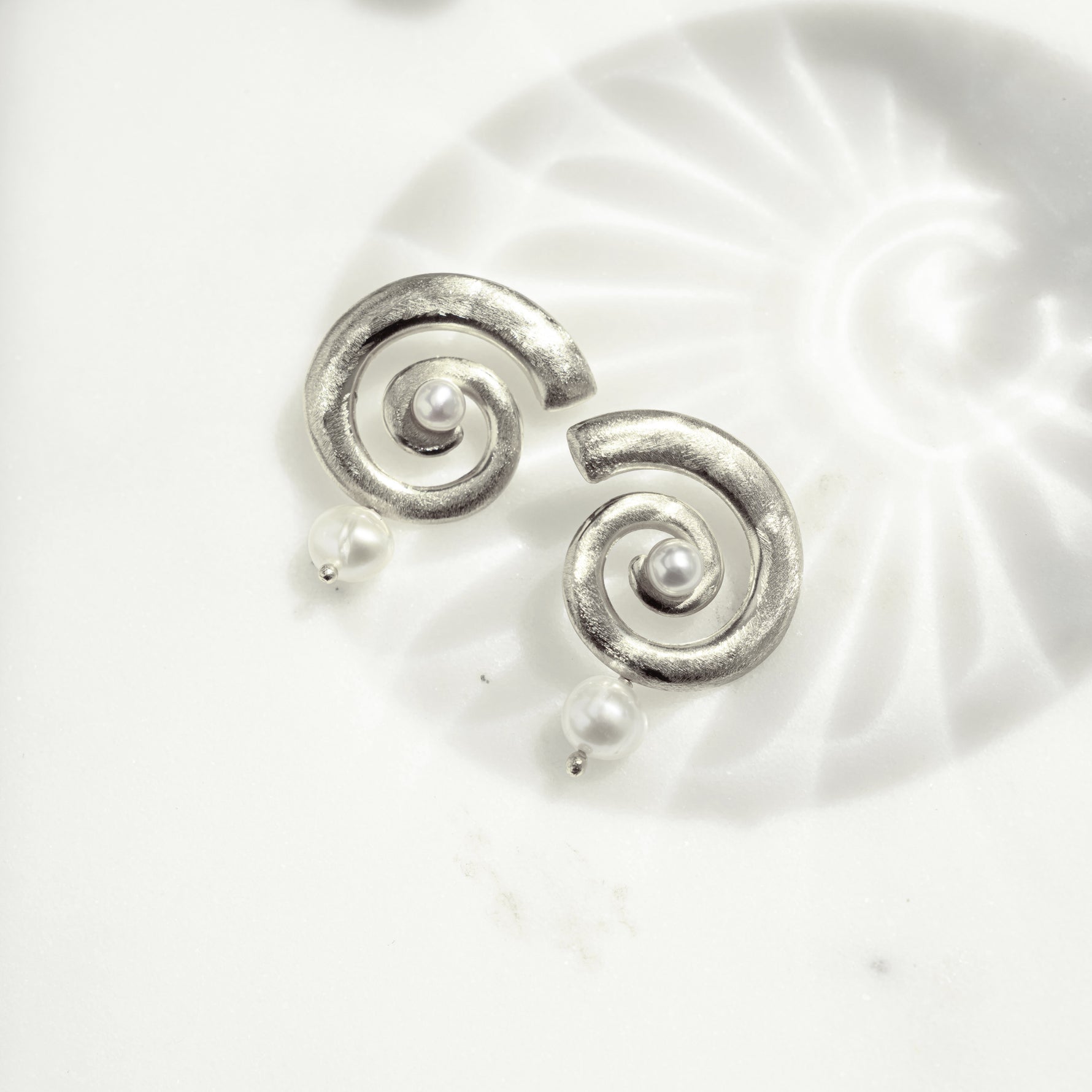 closeup image of silver spiral earrings with a freshwater pearl charm