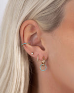 Close-up of a models ear with small gold hoop earrings with turquoise, a mini hoop earring with cubic zirconia stones, a small stud earring, and a turquoise ear cuff