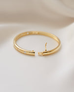 Side view of gold stacking bracelet on a beige fabric background, showcasing its box clasp closure style