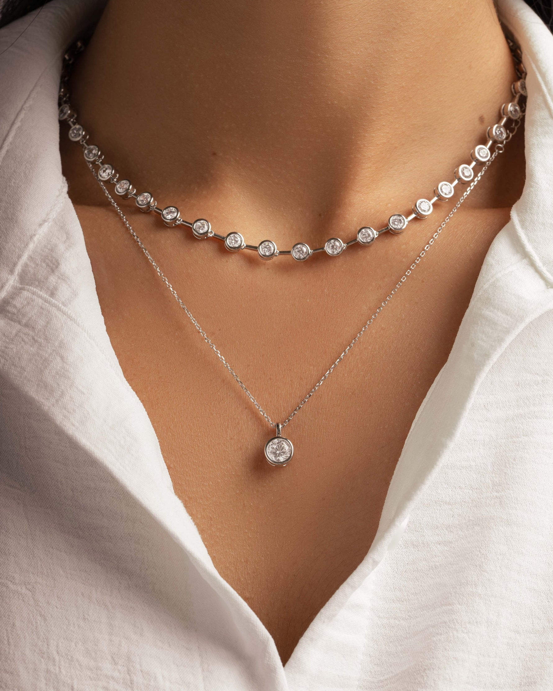 Model wearing layering necklaces featuring a diamond tennis necklace and a delicate necklace with a diamond pendant