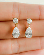 Teardrop-shaped diamond earrings held between fingers on a light background