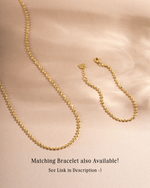 Gold chain layering necklace on beige background with matching gold chain bracelet on beige background