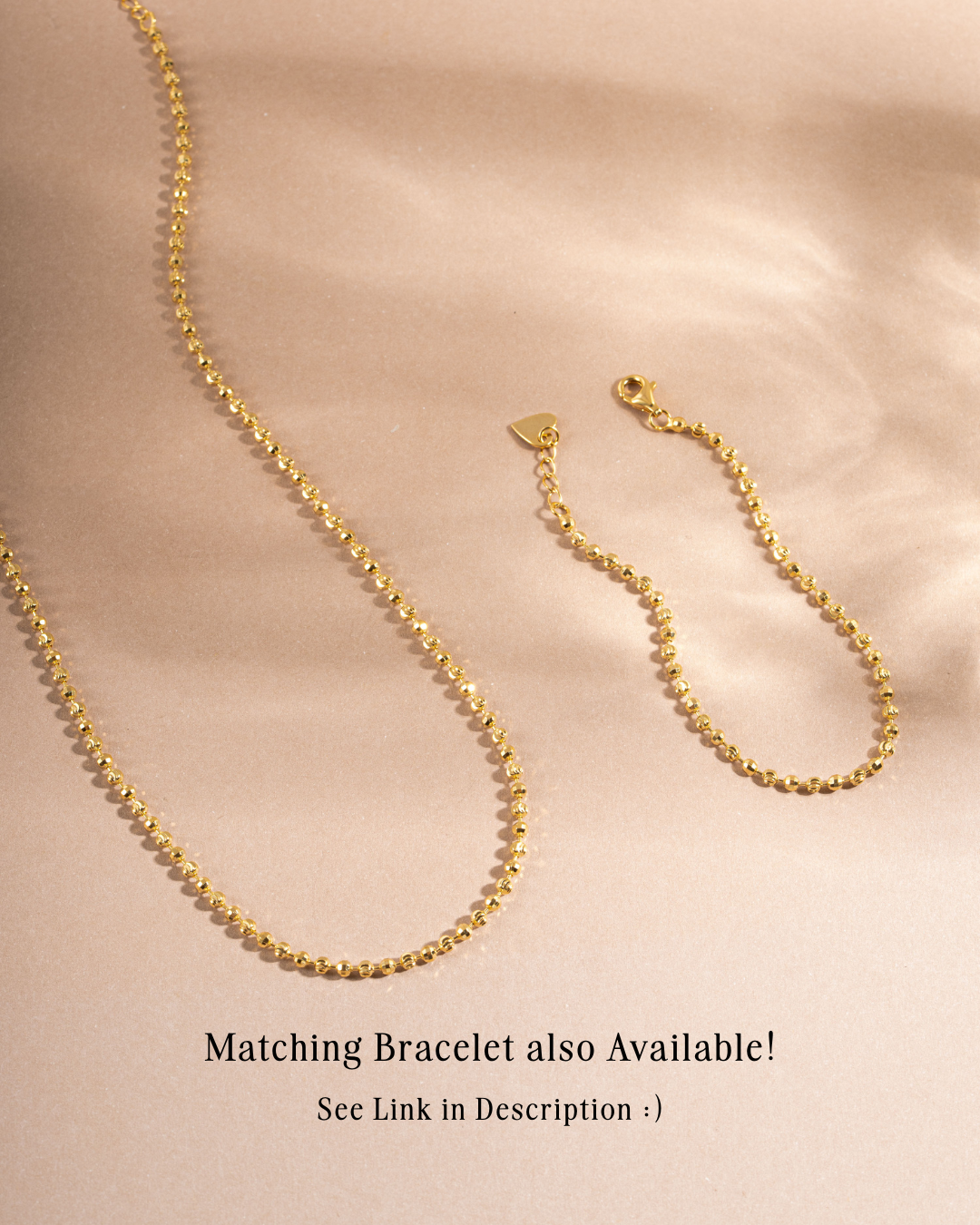 Gold chain layering necklace on beige background with matching gold chain bracelet on beige background