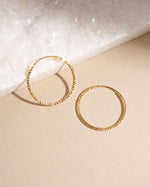 Pair of 32mm gold hoop earrings on beige background, classic everyday gold hoops with subtle diamond sparkle.