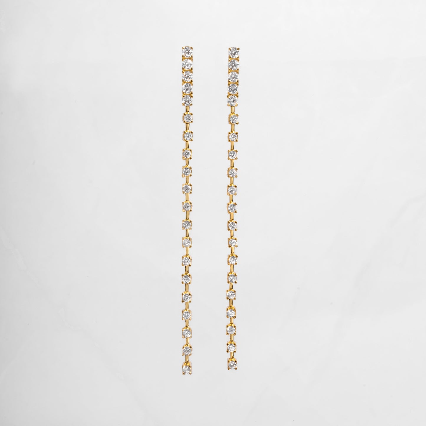 clse up of gold dangle earrings with a smooth, slender line of sparkling cubic zirconia, perfect for bridal earrings or wedding jewelry.