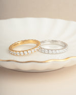 Two diamond rings lying next to eachother on a decorative plate, one gold wedding band with cubic zirconia stones, and one sterling silver dainty ring with cubic zirconia stones