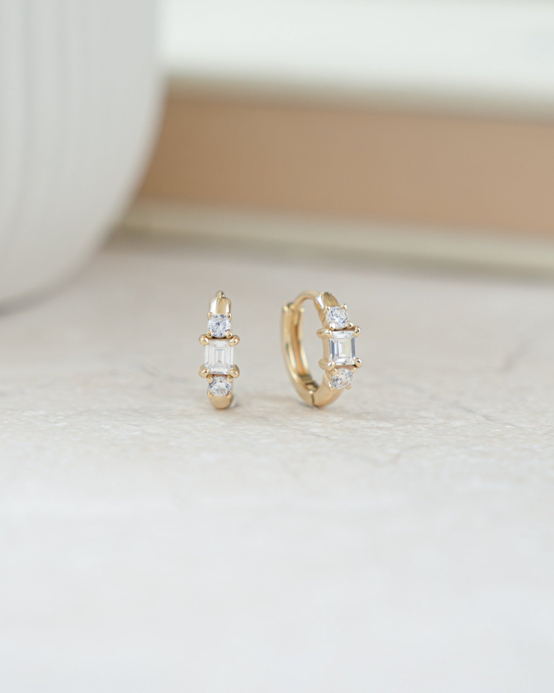 closeup image of gold huggie hoop earrings with three stones 