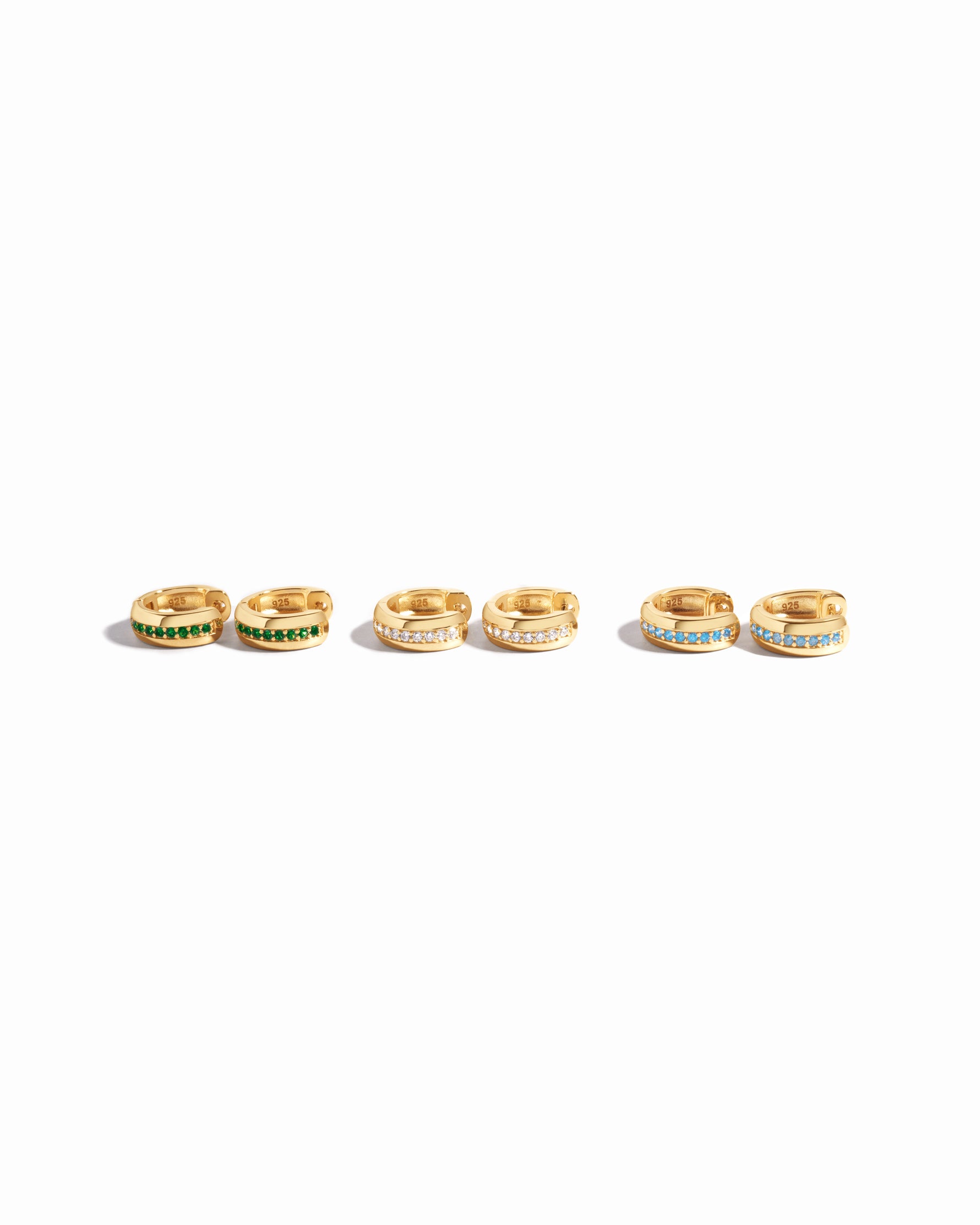 image showcasing our stripe diamond huggie earrings and its different variants including, emerald, white cz, and aquamarine
