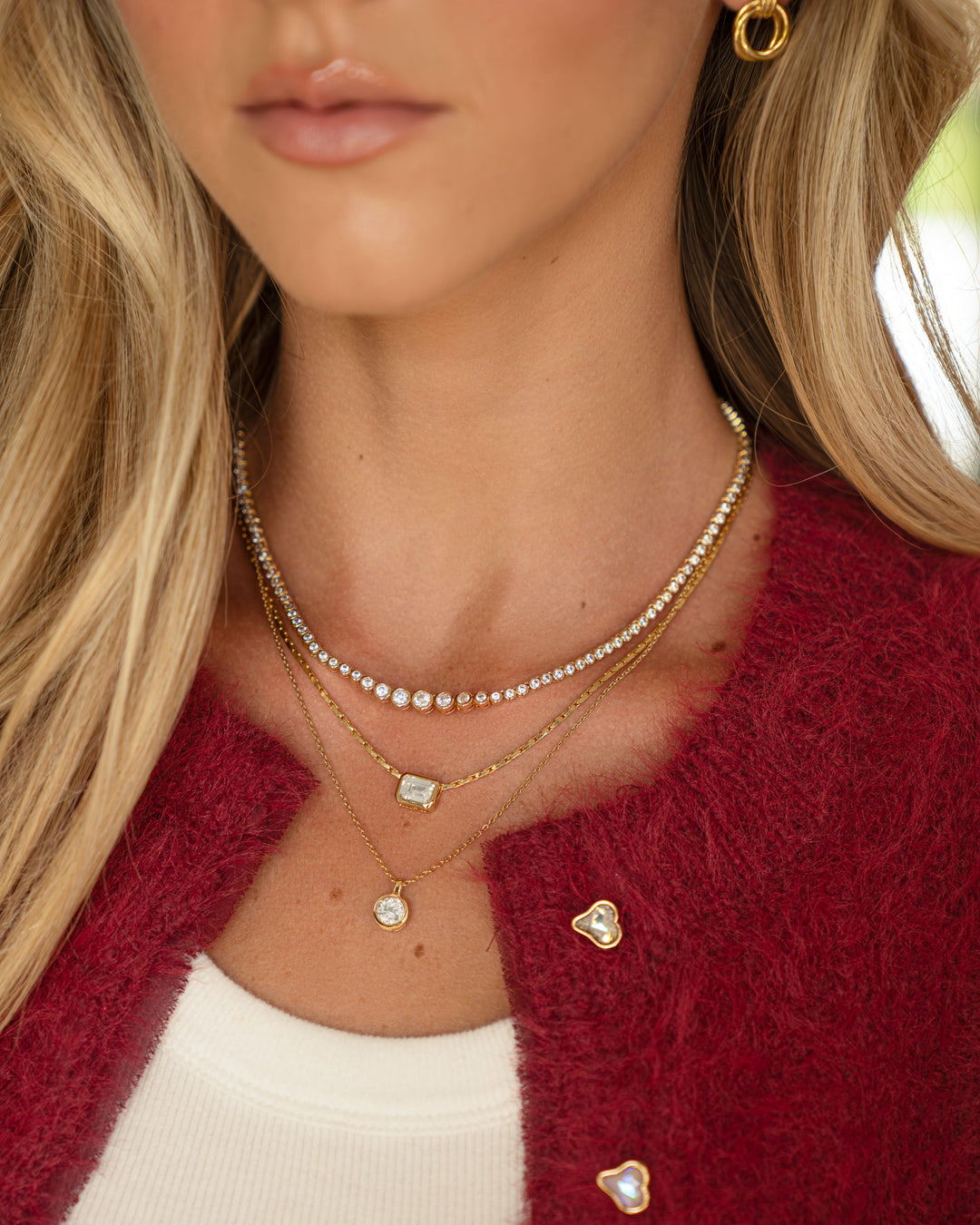 Model wearing gold layering necklaces featuring a gold diamond pendant necklace, a gold emerald cut statement necklace and a a gradient bezel set tennis necklace