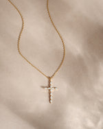 Gold necklace with a cross pendant on a beige background