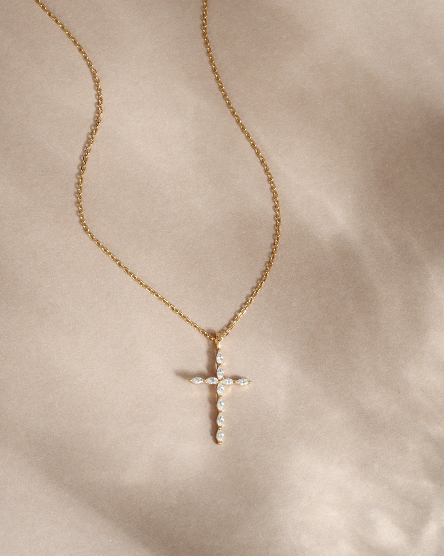 Gold necklace with a cross pendant on a beige background