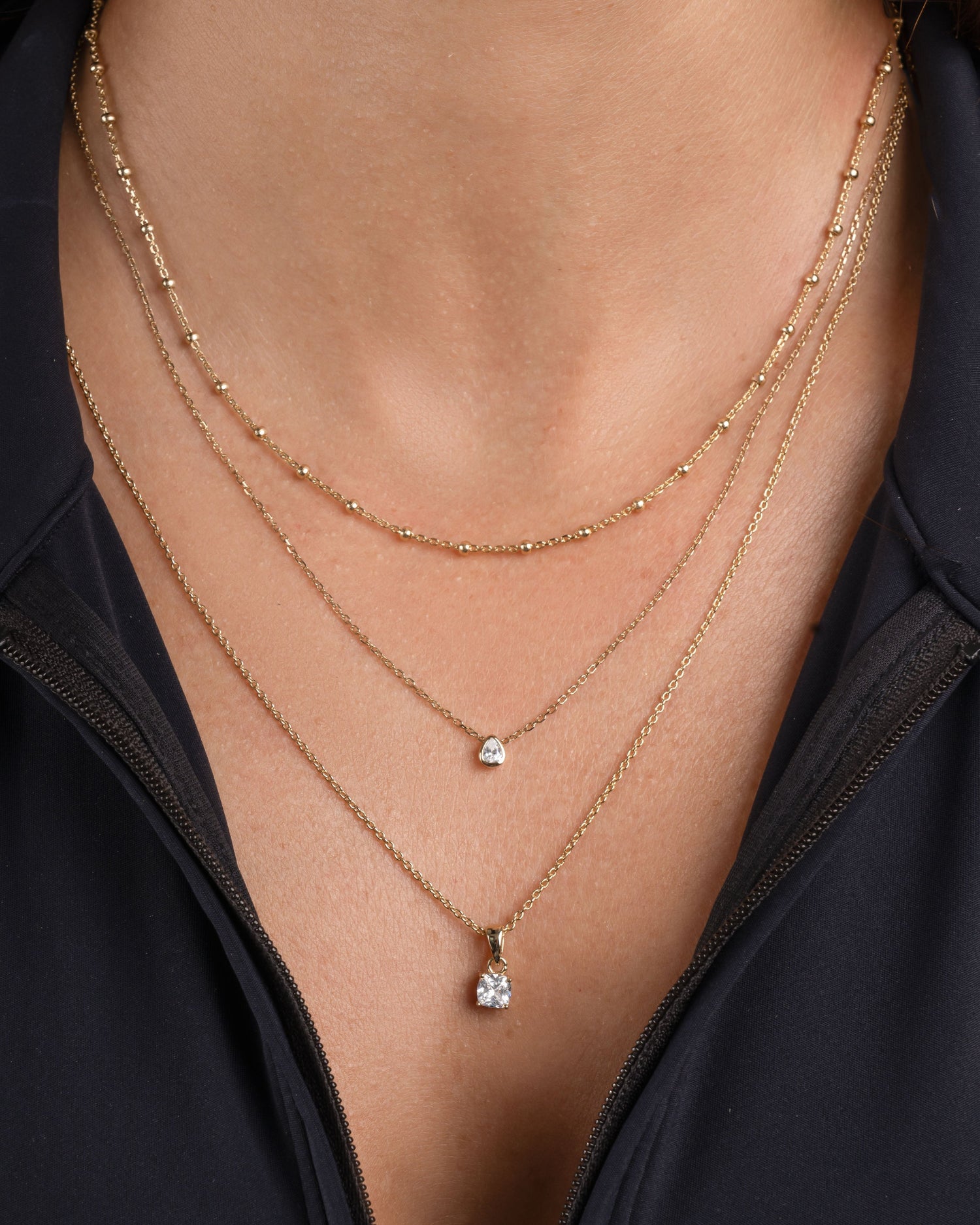 Model wearing gold beaded necklace, a dainty teardrop bezel set necklace and a solitaire diamond pendant necklace
