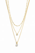 Three gold necklaces on a white background featuring a simple beaded necklace, a gold dainty diamond teardrop pendant necklace, and  another diamond pendant necklace with a solitaire diamond