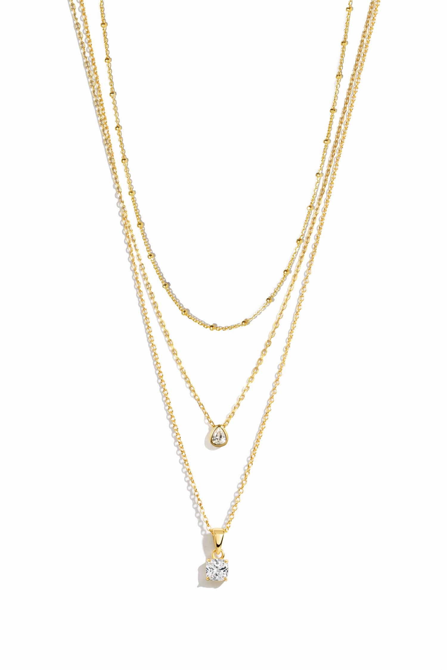 Three gold necklaces on a white background featuring a simple beaded necklace, a gold dainty diamond teardrop pendant necklace, and  another diamond pendant necklace with a solitaire diamond