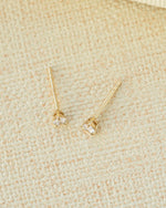 Gold stud earrings with clear gemstones on a beige fabric background