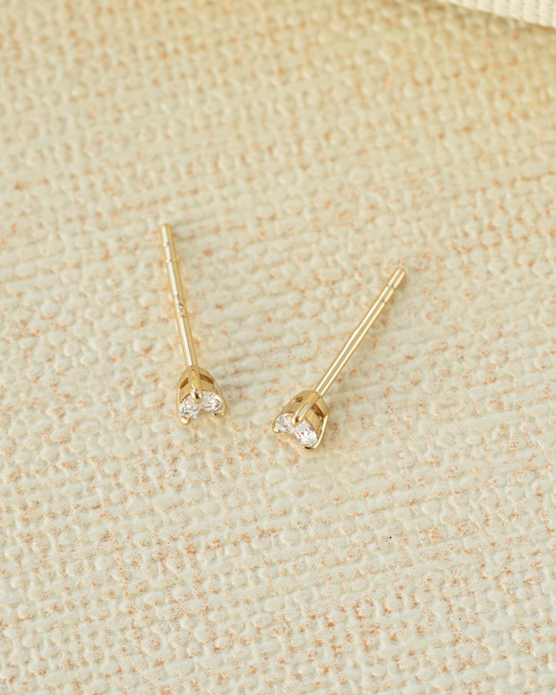Gold stud earrings with clear gemstones on a beige fabric background