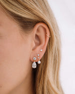 Gold drop earrings, paired with pearl drop earrings, and a pear cut stud earring on model