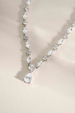 Silver handmade necklace with a pear shaped diamond pendant on a beige background 