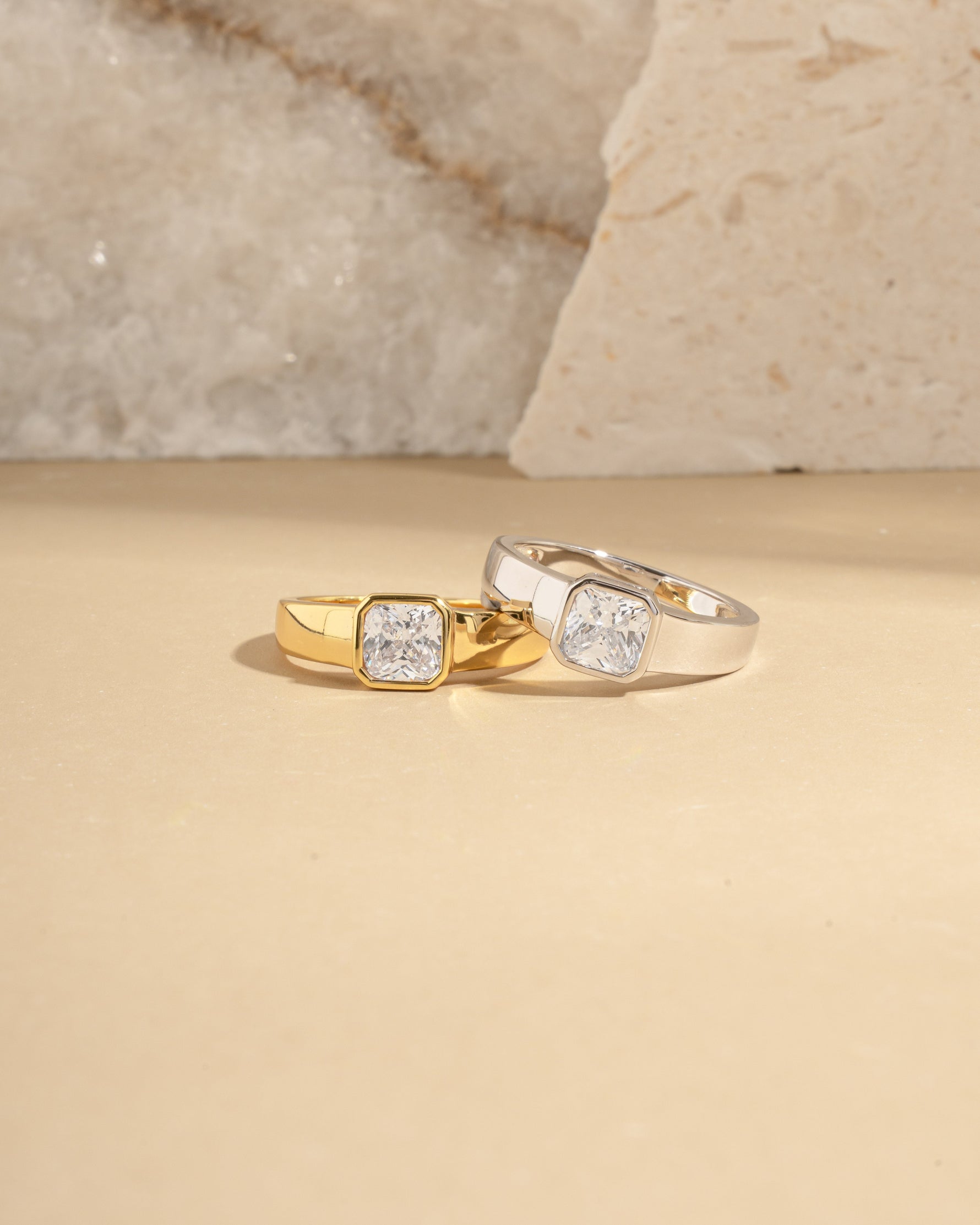 Two gold statements rings with a signet ring design and bezel set diamond on a beige surface.