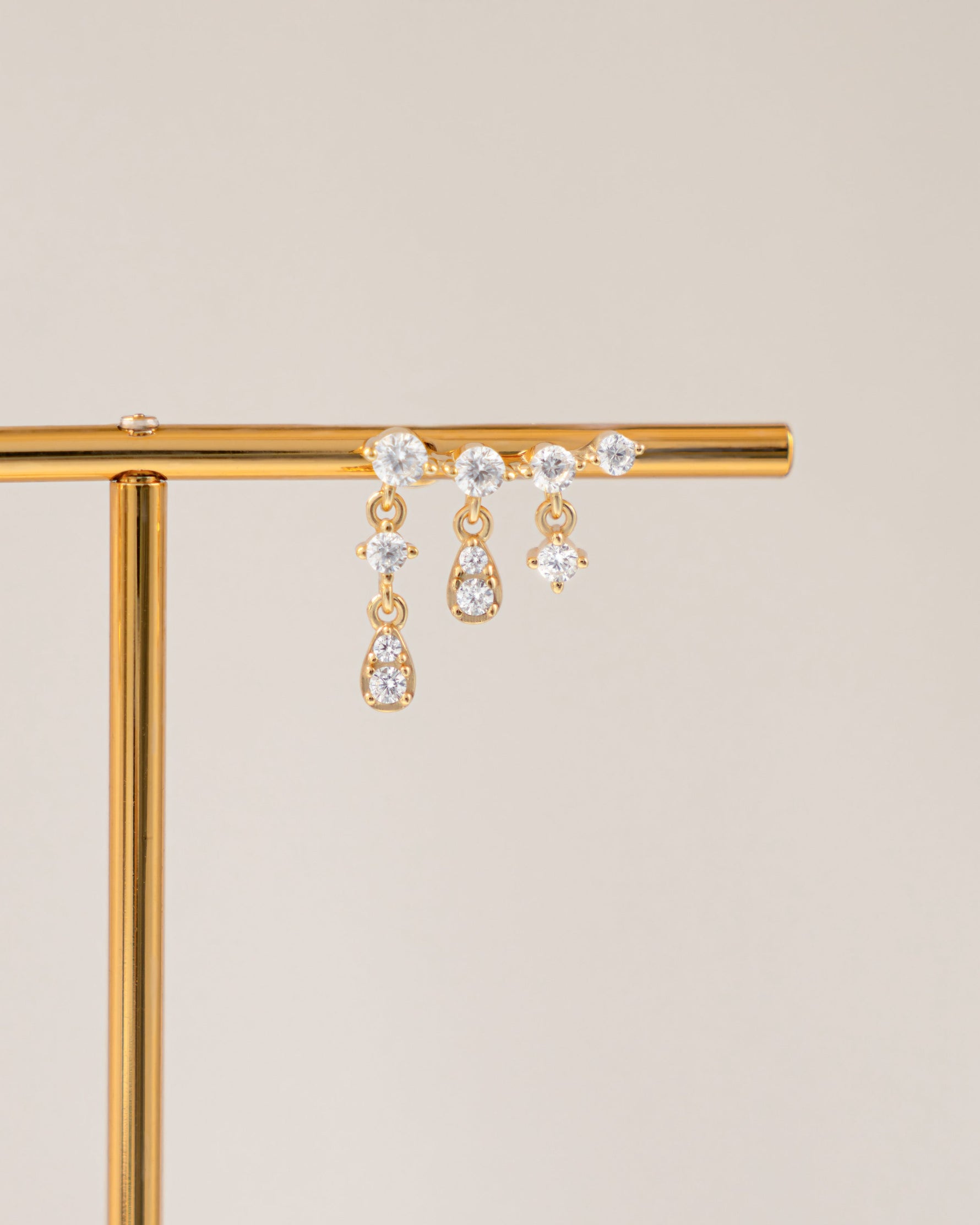 Gold dainty earring on a gold stand against a beige background