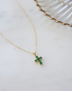 Gold necklace with a green gemstone cross pendant on a white surface