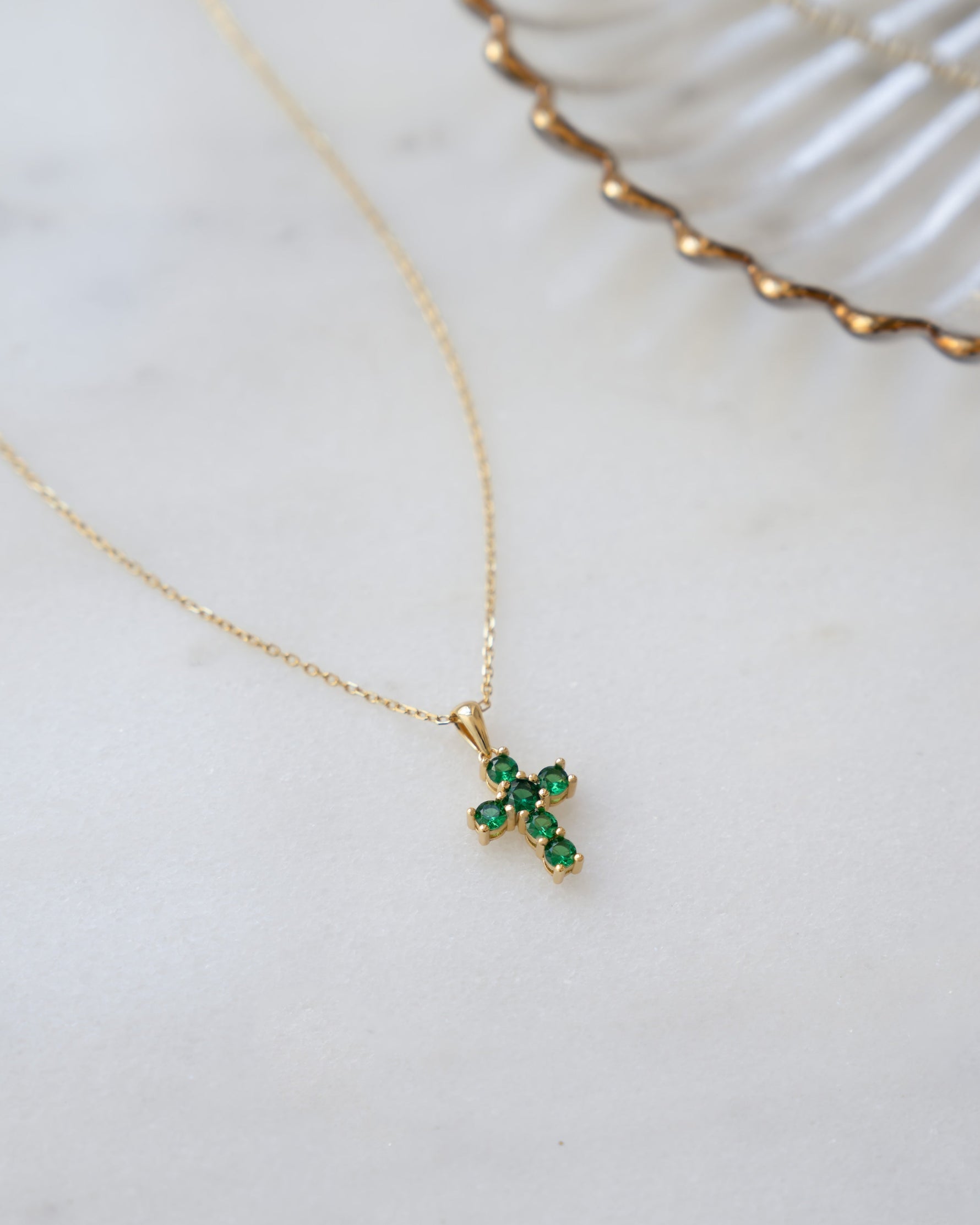 Gold necklace with a green gemstone cross pendant on a white surface