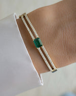 Diamond bangle with a emerald gemstone on a wrist against a white background