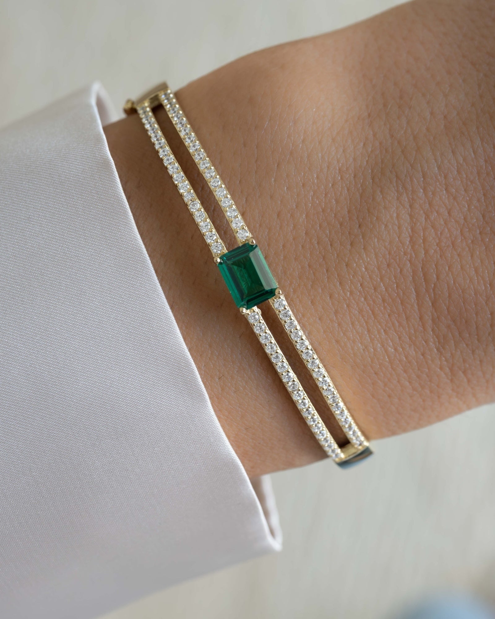 Diamond bangle with a emerald gemstone on a wrist against a white background