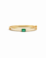Gold bangle bracelet with a emerald green gemstone on a white background