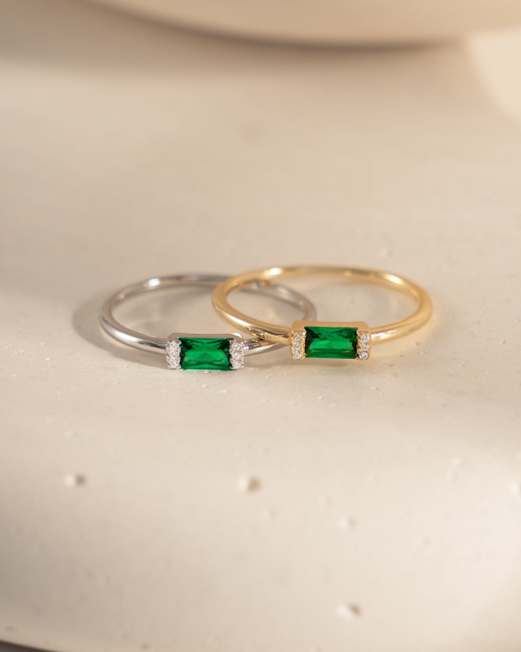 closeup image of sterling silver emerald baguette ring and 14k gold plated emerald green ring