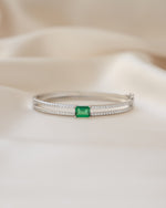 Silver bangle with a green gemstone on a beige fabric background