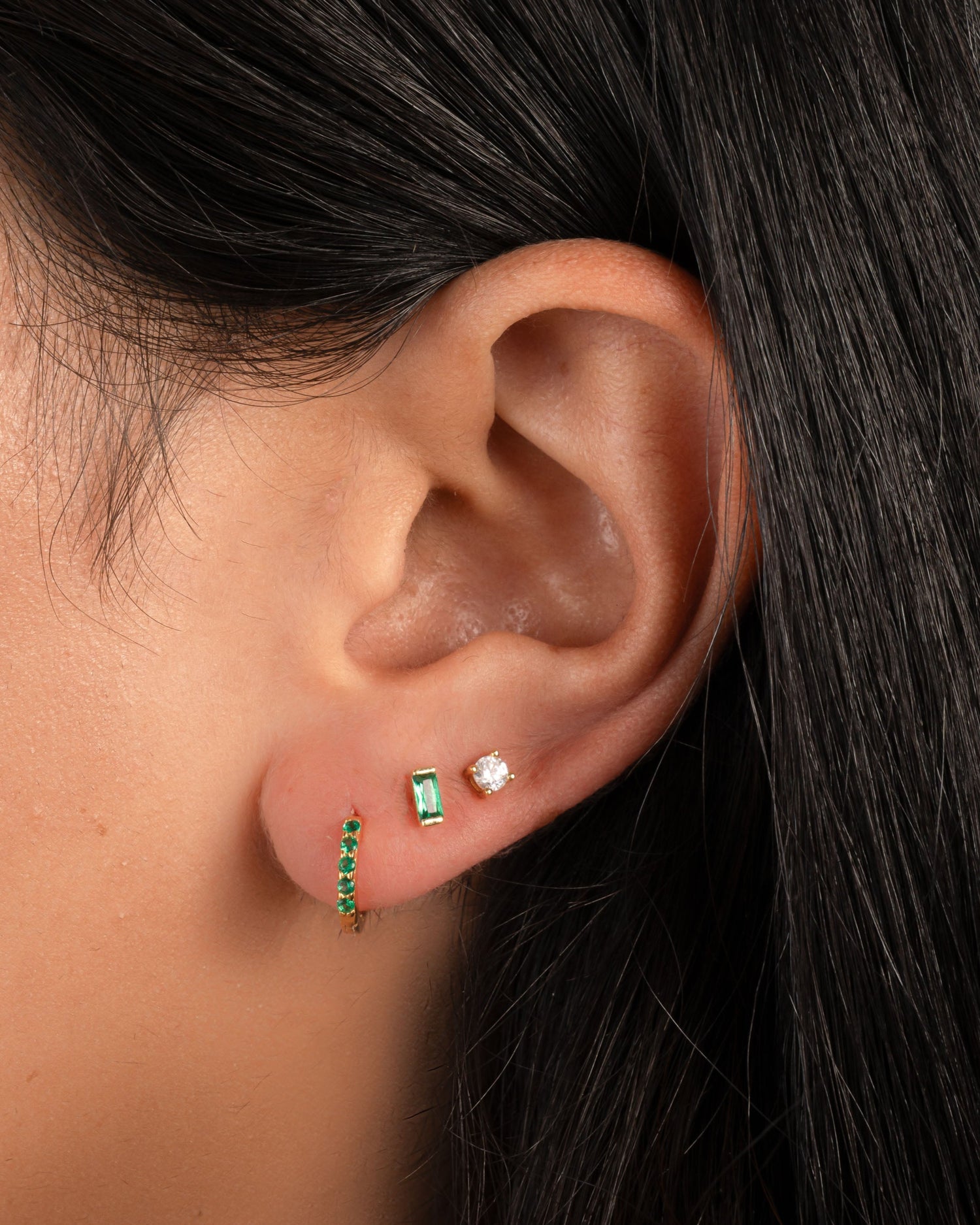 model wearing emerald green huggie hoop earrings with emerald green stone stud earring and a classic round soliatire stud