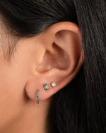 model wearing silver hoop earrings featuring an emerald green huggie hoop earring, a green baguette stud, and a solitaire stud earring