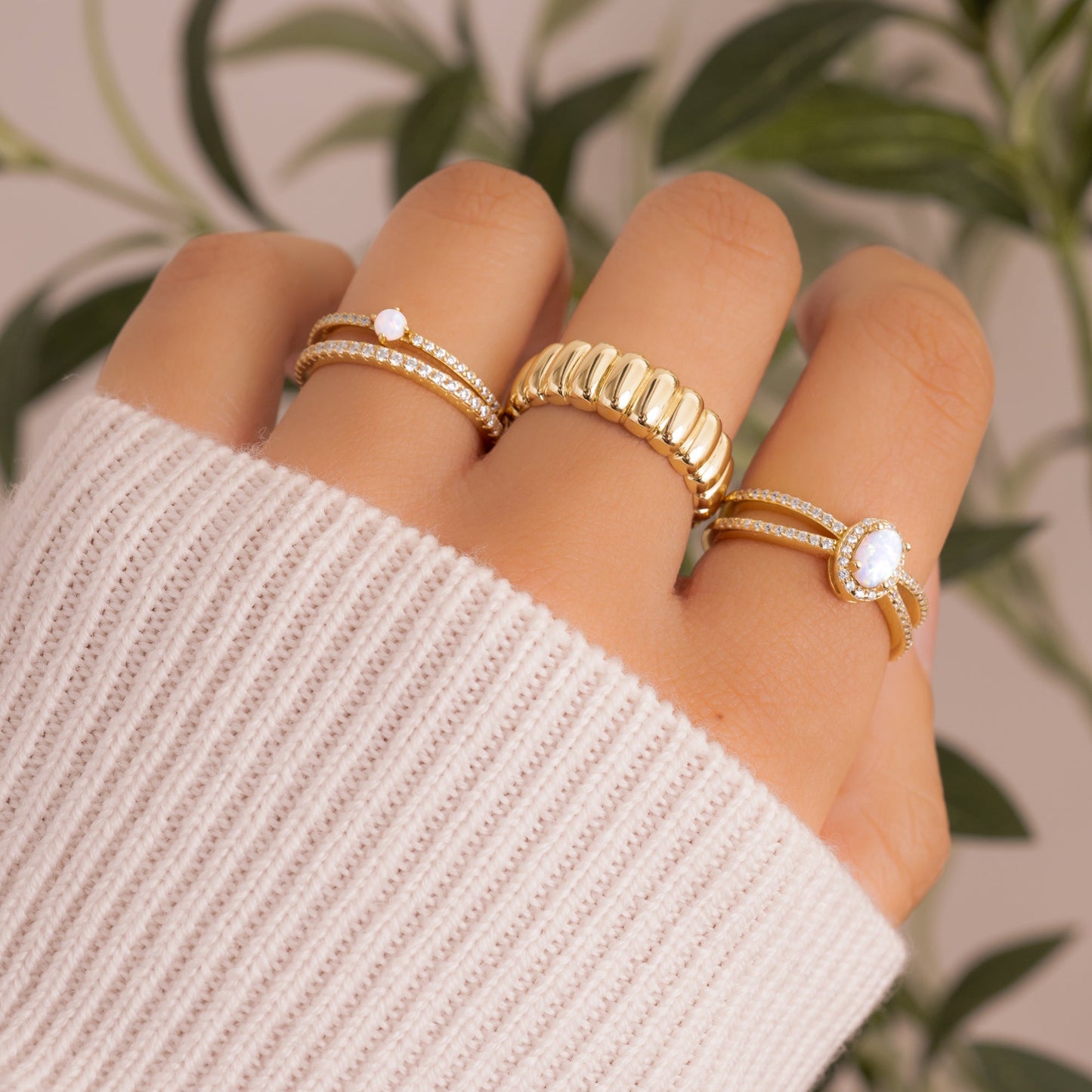 model wearing gold rings featuring a cubic zirconia stone diamond eternity band, and opal solitaire stone on an cz eternity band, a gold statement ring, and an opal oval statement ring.