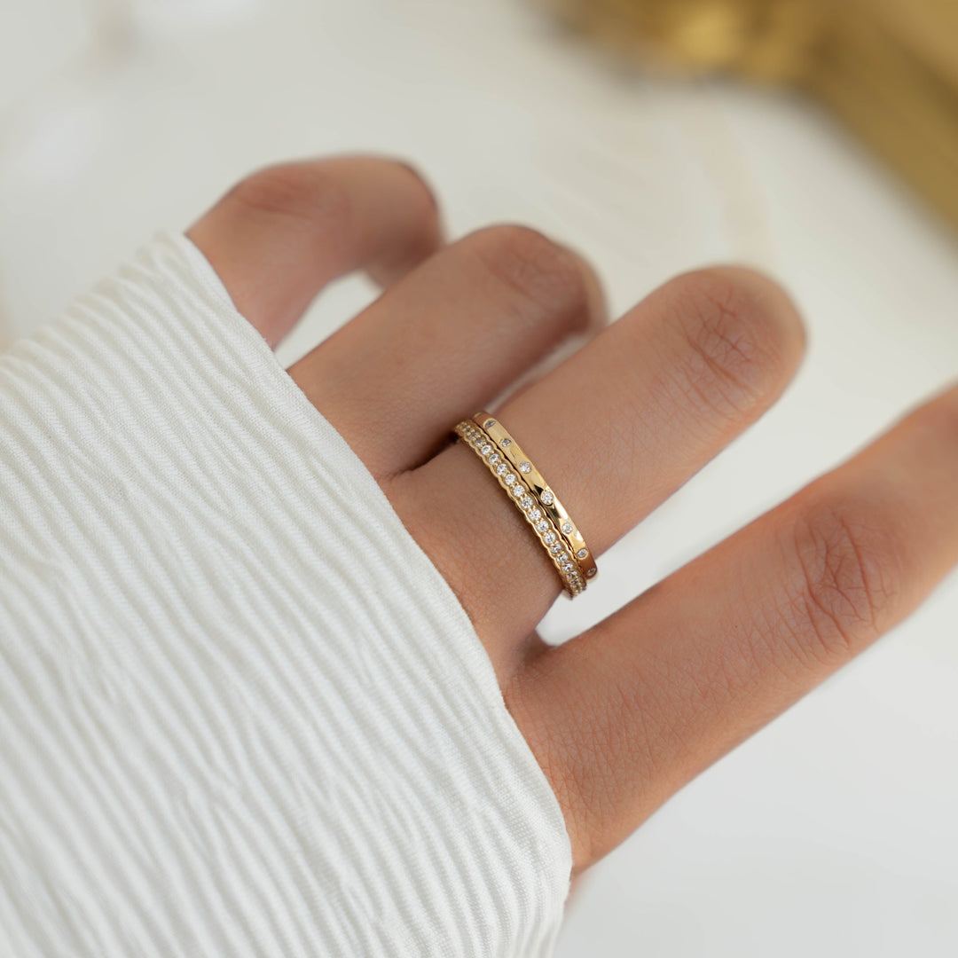 Two Sami Jewels eternity rings set, featuring intertwined gold bands with sparkling gemstone accents on a white background.