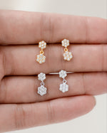 Tiny earrings with a charm earring design displayed on a hand against a neutral background